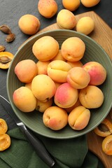 Fresh ripe apricots in bowl and knife on black table, flat lay
