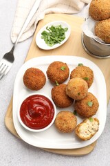 Delicious fried croquette balls with parsley and ketchup served on grey textured table, flat lay