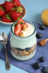 Tasty yogurt with granola, berries and honey on light blue wooden table, closeup