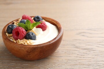 Tasty yogurt with granola and berries in bowl on wooden table, closeup. Space for text