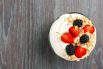 Tasty yogurt with granola and berries in bowl on wooden table, top view. Space for text