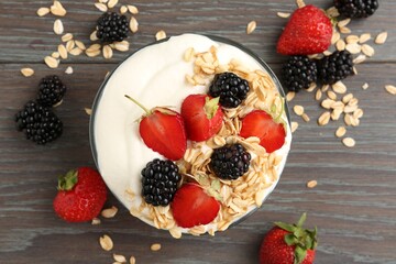 Tasty yogurt with granola and berries in bowl on wooden table, flat lay