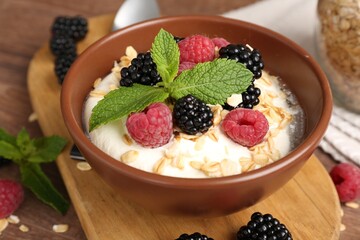 Tasty yogurt with granola and berries in bowl on wooden table, closeup
