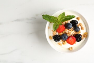 Tasty yogurt with granola and berries in bowl on white marble table, top view. Space for text