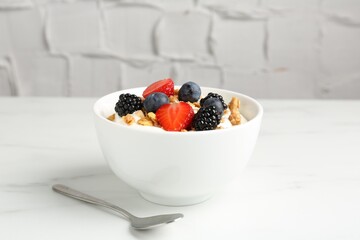 Tasty yogurt with granola and berries in bowl on white marble table, closeup
