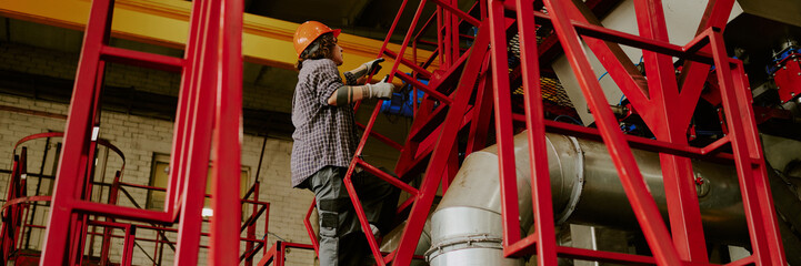Website banner of woman wearing safety helmet working on industrial scaffolding, using tools to...