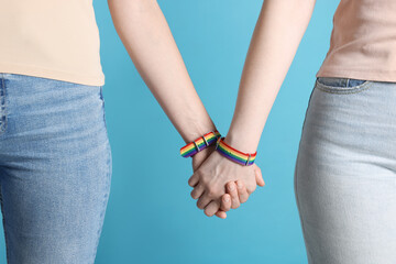 LGBT concept. Women in rainbow wristbands holding hands on light blue background, closeup