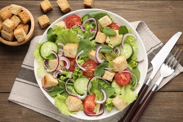 Delicious salad with croutons and vegetables on wooden table, flat lay