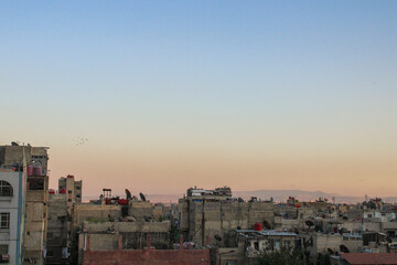 Damascus, Syria - JULY 10, 2024: A landscape view of a neighborhood in Damascus, Syria at sunset with a flock of birds in the sky
