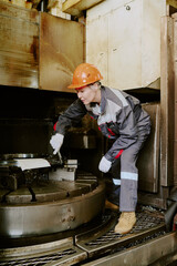 Young adult Caucasian woman operating industrial machinery in factory setting, wearing protective...