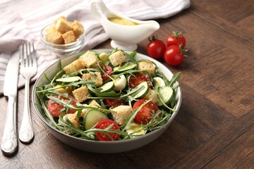 Tasty salad with croutons, cucumbers, tomatoes and arugula on wooden table, closeup. Space for text