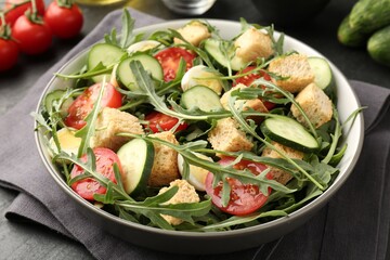 Tasty salad with croutons, cucumbers, tomatoes and arugula on black table, closeup
