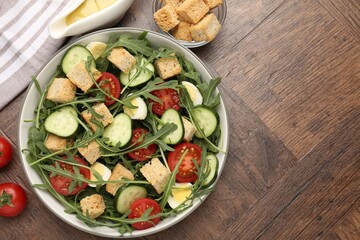 Tasty salad with croutons, cucumbers, tomatoes and arugula on wooden table, flat lay. Space for text