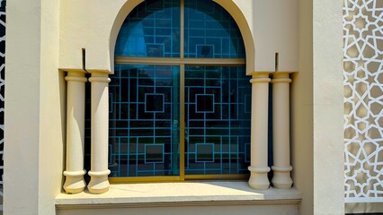 Intricate blue glass window with geometric pattern stands between symmetrical columns outside building