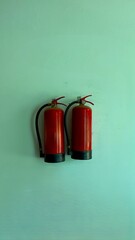 Two red fire extinguishers are mounted together on a light green painted wall