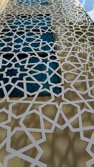 White geometric lattice pattern adorns a building facade obscuring windows viewed from a low angle
