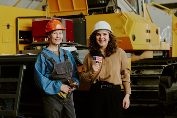 Caucasian middle aged woman wearing hard hat standing next to Caucasian young adult woman holding...