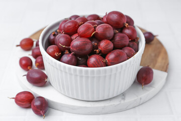 Ripe red gooseberries in bowl on white tiled table, closeup