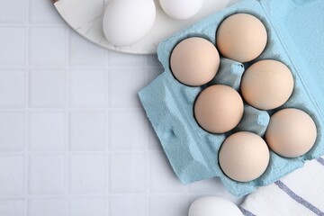 Raw chicken eggs in egg carton on white tiled table, flat lay. Space for text