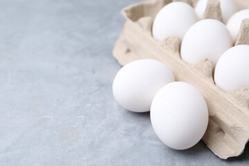 Raw chicken eggs in egg carton on grey table, closeup. Space for text