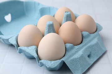 Raw chicken eggs in egg carton on white tiled table, closeup