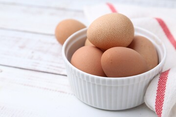 Raw chicken eggs in bowl on white wooden table, closeup. Space for text