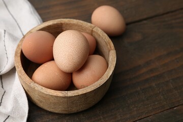 Raw chicken eggs in bowl on wooden table, closeup. Space for text
