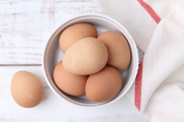 Raw chicken eggs in bowl on white wooden table, top view