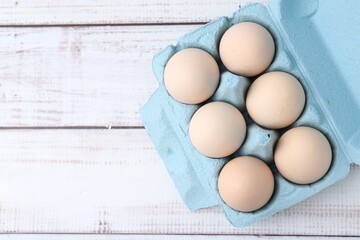 Raw chicken eggs in egg carton on white wooden table, top view. Space for text