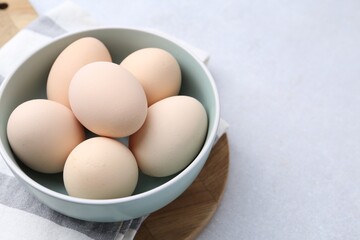 Raw chicken eggs in bowl on white table, closeup. Space for text