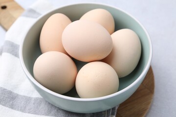 Raw chicken eggs in bowl on white table, closeup