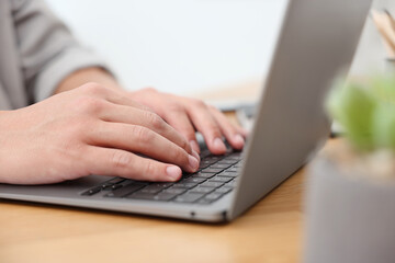 Copywriter using laptop at wooden table indoors, closeup