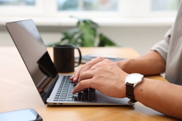 Copywriter using laptop at wooden table indoors, closeup