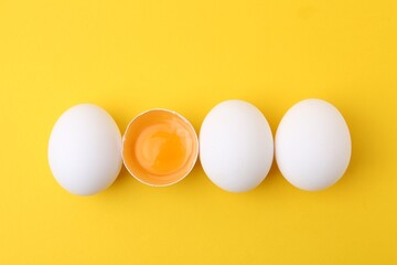 Whole and broken chicken eggs on yellow background, top view