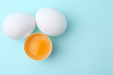 Whole and broken chicken eggs on light blue background, top view. Space for text