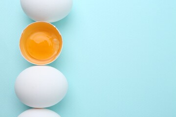 Whole and broken chicken eggs on light blue background, top view. Space for text
