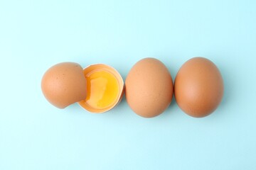 Whole and broken chicken eggs on light blue background, top view