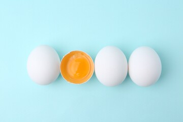 Whole and broken chicken eggs on light blue background, top view