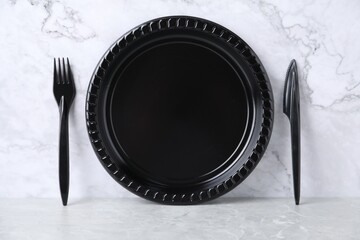 Disposable plastic plate, knife and fork on light grey table