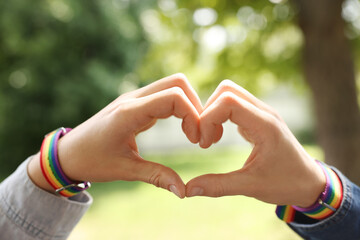 LGBT concept. Women in rainbow wristbands making heart shape outdoors, closeup