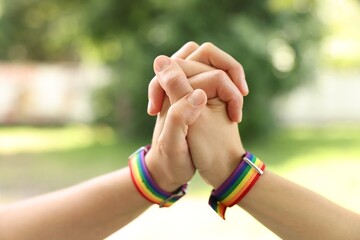 LGBT concept. Women in rainbow wristbands holding hands outdoors, closeup