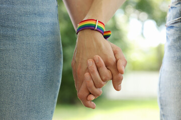LGBT concept. Women in rainbow wristbands holding hands outdoors, closeup