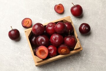 Ripe cherry plums and wooden crate on grey textured table, flat lay