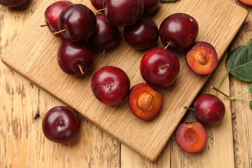 Ripe cherry plums and board on wooden table, flat lay