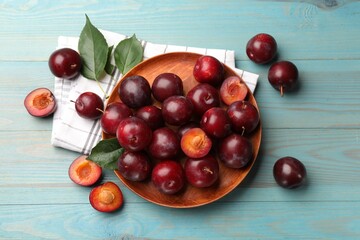 Whole, cut cherry plums, cloth and green leaves on light blue wooden table, flat lay