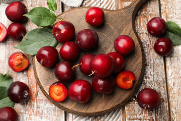 Whole, cut cherry plums and green leaves on color wooden table, flat lay