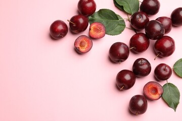 Whole, cut cherry plums and green leaves on pink background, flat lay. Space for text