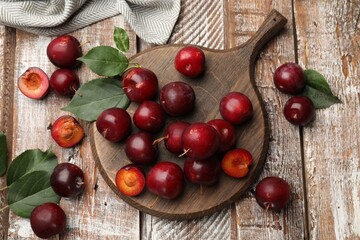 Whole, cut cherry plums and green leaves on color wooden table, flat lay