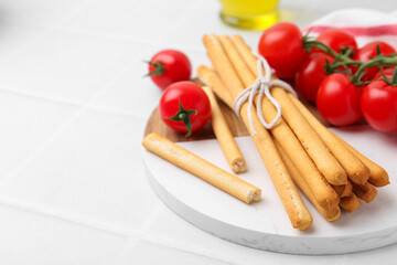 Delicious grissini sticks and fresh tomatoes on white tiled table, closeup. Space for text