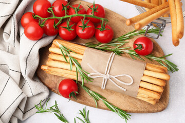 Delicious grissini sticks, rosemary and fresh tomatoes on light grey table, flat lay